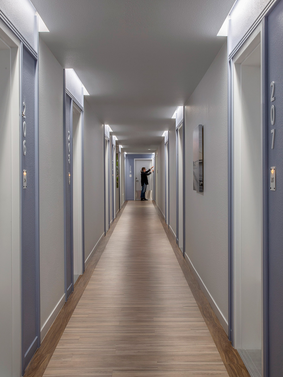Fixed-length cove lights over each apartment entry door in a hallway provide an upscale feel to an affordable housing project in Palo Alto, California.