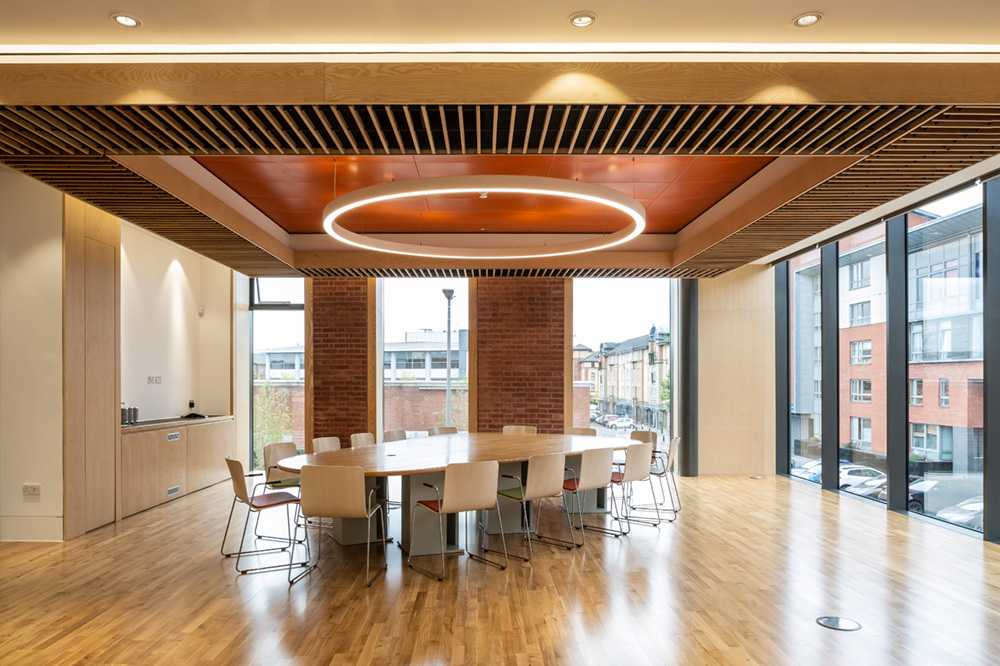 Modern LED ring pendant light suspended from a recessed ceiling over an office conference room table