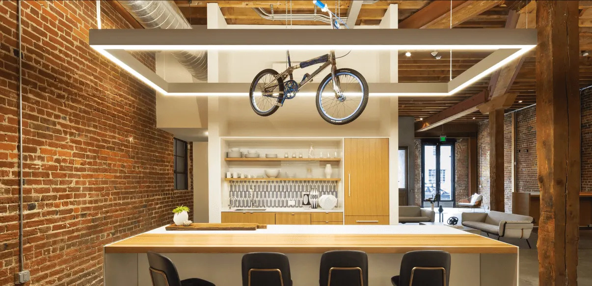 A square linear pendant LED light hangs over a bar area with a bicycle suspended in the center
